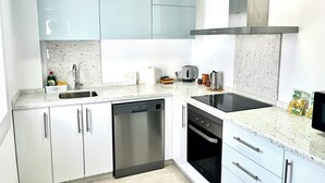 Une cuisine moderne avec des meubles blancs, un lave-vaisselle, un four, une plaque de cuisson et une machine à café.
