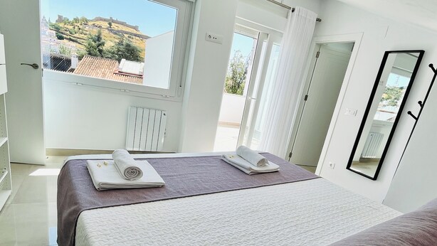 Une chambre d’hôtel avec un lit, une fenêtre donnant sur une colline, un radiateur et un miroir au mur.