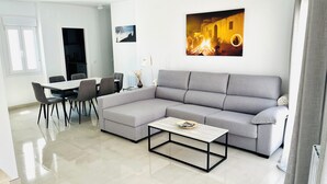 Un salon moderne avec un canapé d’angle gris, une table à manger avec des chaises et une table basse.