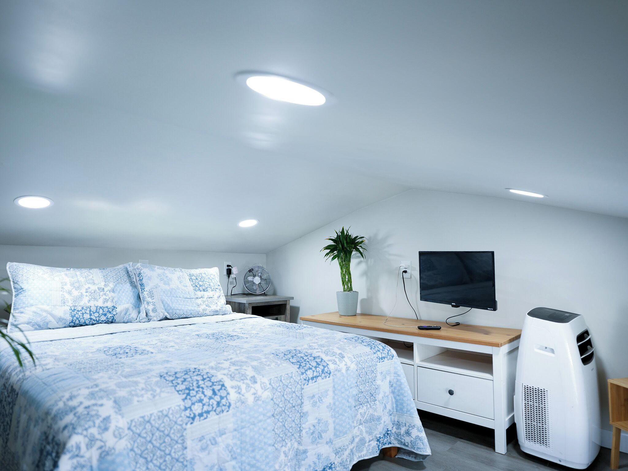 A modern bedroom with a bed, a desk, a TV, and a white air purifier.