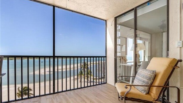 A balcony with a view of the beach, a cushioned chair, and a glass door leading to an interior space.