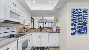 A modern kitchen with white cabinetry, a built-in oven, and a central island with a sink.