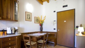 Une petite cuisine avec des meubles en bois, une table à manger avec des chaises, une machine à café et un vase rempli de fleurs.