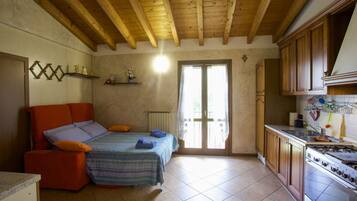 A cozy bedroom with a bed, a small sofa, and a kitchenette with a stove.