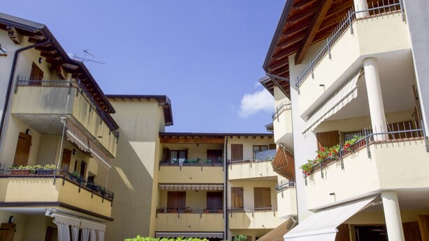 Une cour intérieure bordée d’immeubles à plusieurs étages, dotés de balcons avec des garde-corps et de plantes en pot.