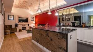 A modern kitchen with a red accent wall, a marble island, and pendant lighting.