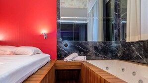 A modern bathroom with a wooden bench, a large bathtub, and a red wall.