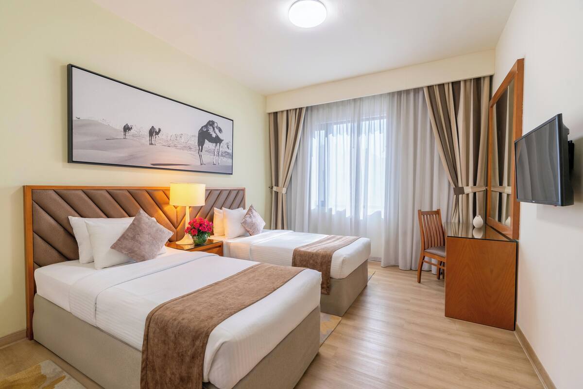 Une chambre d’hôtel avec deux lits, une télévision, un bureau et un tableau représentant un paysage désertique.