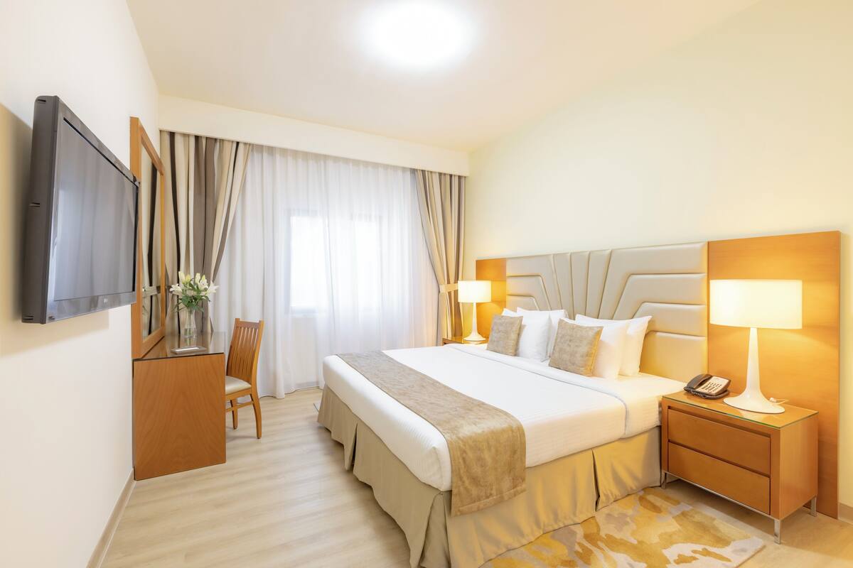 Une chambre d’hôtel avec un grand lit, des lampes de chevet, un bureau avec une chaise, un téléviseur à écran plat et une fenêtre avec des rideaux.