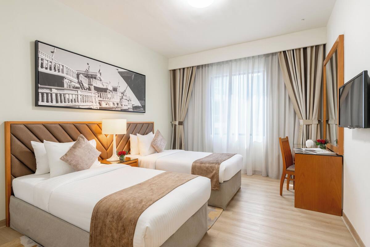 Une chambre d’hôtel avec deux lits, un bureau, une chaise, une télévision et un grand tableau encadré au mur.