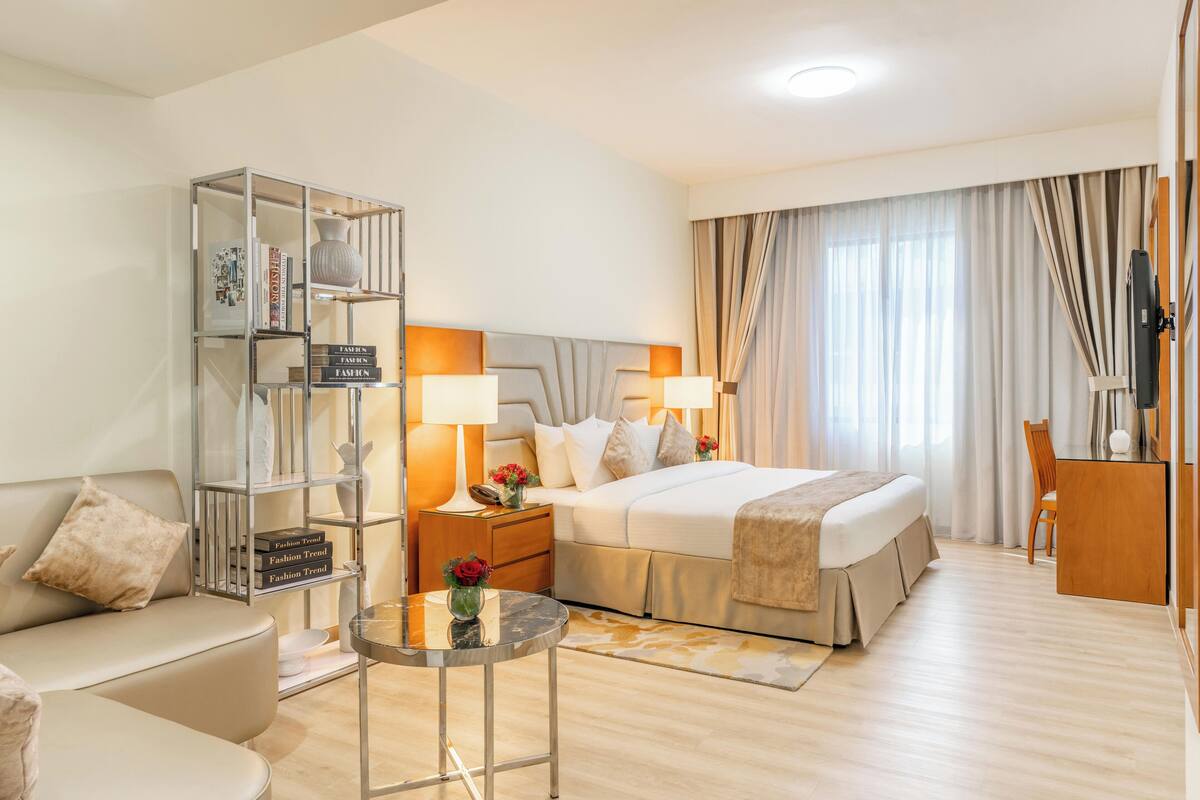 Une chambre d’hôtel comprenant un lit, un canapé, une table de chevet avec des lampes, une petite table et un téléviseur.