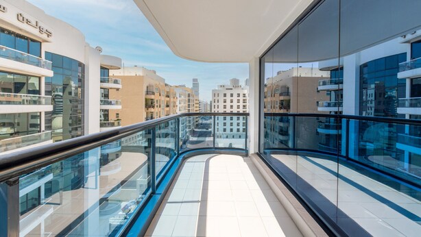 Un bâtiment moderne doté d’un balcon en verre et offrant une vue sur d’autres immeubles.