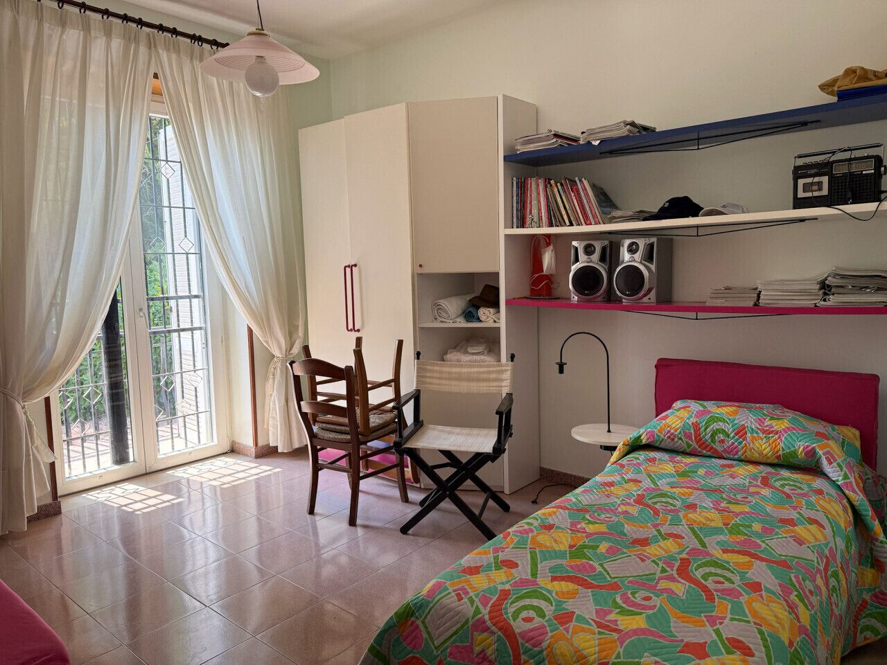 Un dormitorio con cama, escritorio, silla, armario y ventana con cortinas.