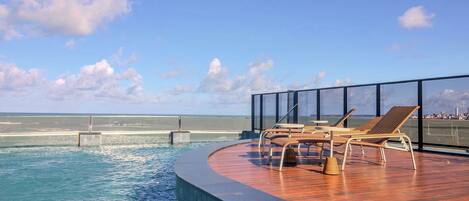 Zona de piscina con sillones de descanso y vistas al mar.