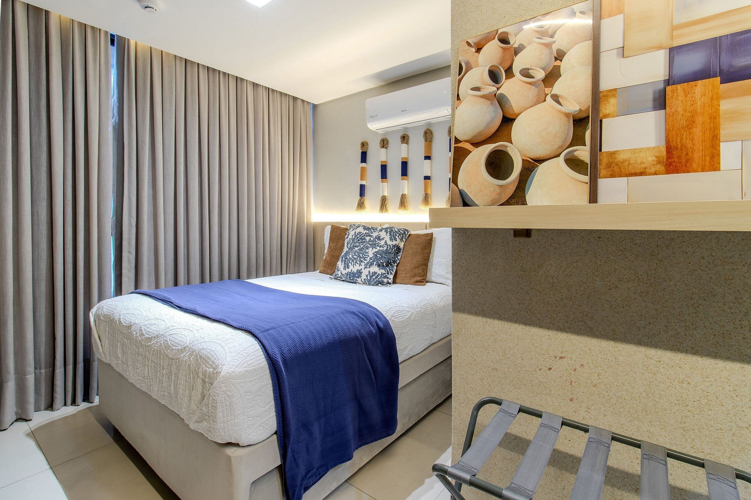 A hotel room with a bed, curtains, an air conditioning unit, and a wall with pottery.