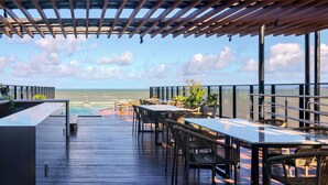 A wooden deck with outdoor seating, a pool, and a view of the ocean. - Alta Marine (João Pessoa)