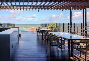 Una terraza de madera con mobiliario exterior, piscina y vista al océano.