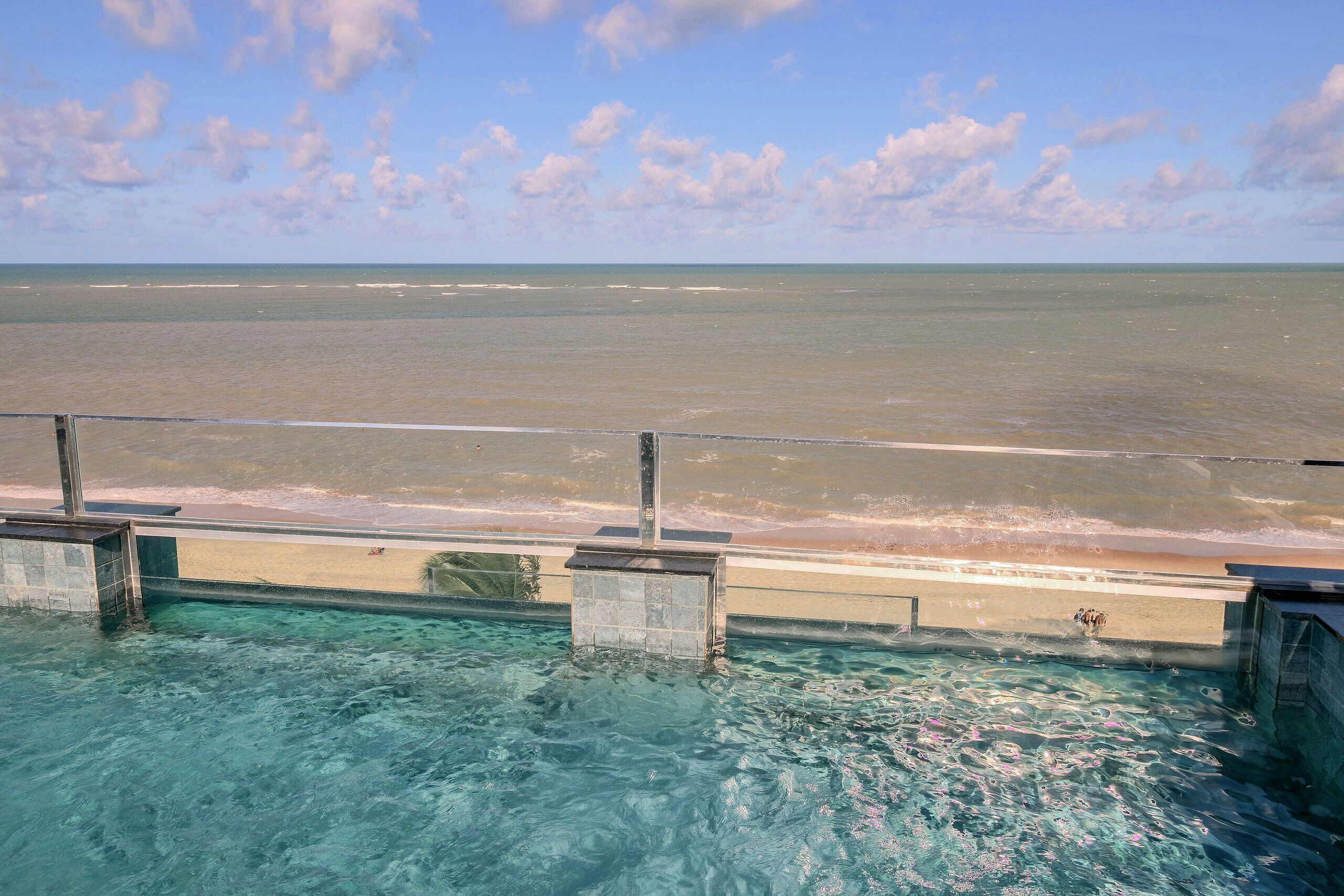 A clear view of the ocean from a poolside area with a metal railing.