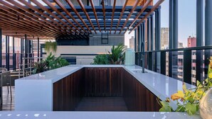 A modern outdoor bar area with a wooden ceiling, large windows, and potted plants. - Alta Marine (João Pessoa)