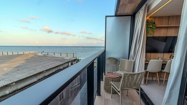 A balcony with a view of the sea, wicker chairs, a small table, and a TV. - Alta Marine (João Pessoa)