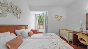 Une chambre d’hôtel avec deux lits, un bureau, une chaise et une fenêtre donnant sur un espace verdoyant.
