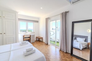 A hotel room with two beds, a desk, a chair, and a balcony with a view.