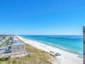 A coastal view with a beach, a row of houses, and a clear blue sky.