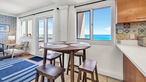 A kitchen with a round table, bar stools, a view of the ocean, and a balcony.
