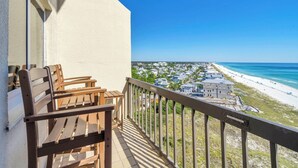 A balcony with wooden chairs and a view of a beach and buildings.