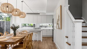 Una cocina moderna con armarios blancos, una mesa de comedor de madera con individuales tejidos y una escalera con barandillas blancas.