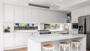 Una cocina moderna con armarios blancos, una isla central con taburetes, un refrigerador de acero inoxidable y un ventanal con vistas a zonas verdes.