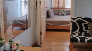 A compact room with a bed, a sitting area with a chair, a small table, and a mirror. - Azure Urban Resort Residences (Parañaque)