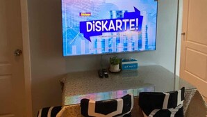 A dining area with a TV displaying a news channel, a framed abstract artwork, and a table with patterned chairs. - Azure Urban Resort Residences (Parañaque)