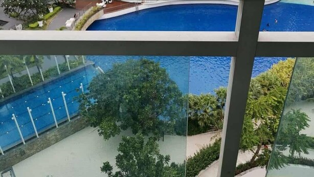 A modern building with a curved roof, a swimming pool, and a view of surrounding high-rise buildings. - Azure Urban Resort Residences (Parañaque)