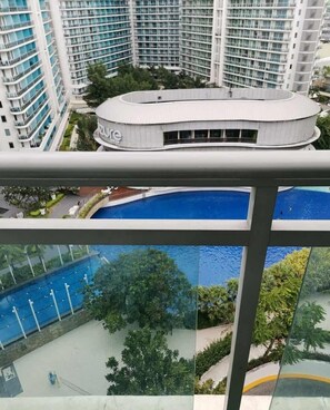 A modern building with a curved roof, a swimming pool, and a view of surrounding high-rise buildings. - Azure Urban Resort Residences (Parañaque)