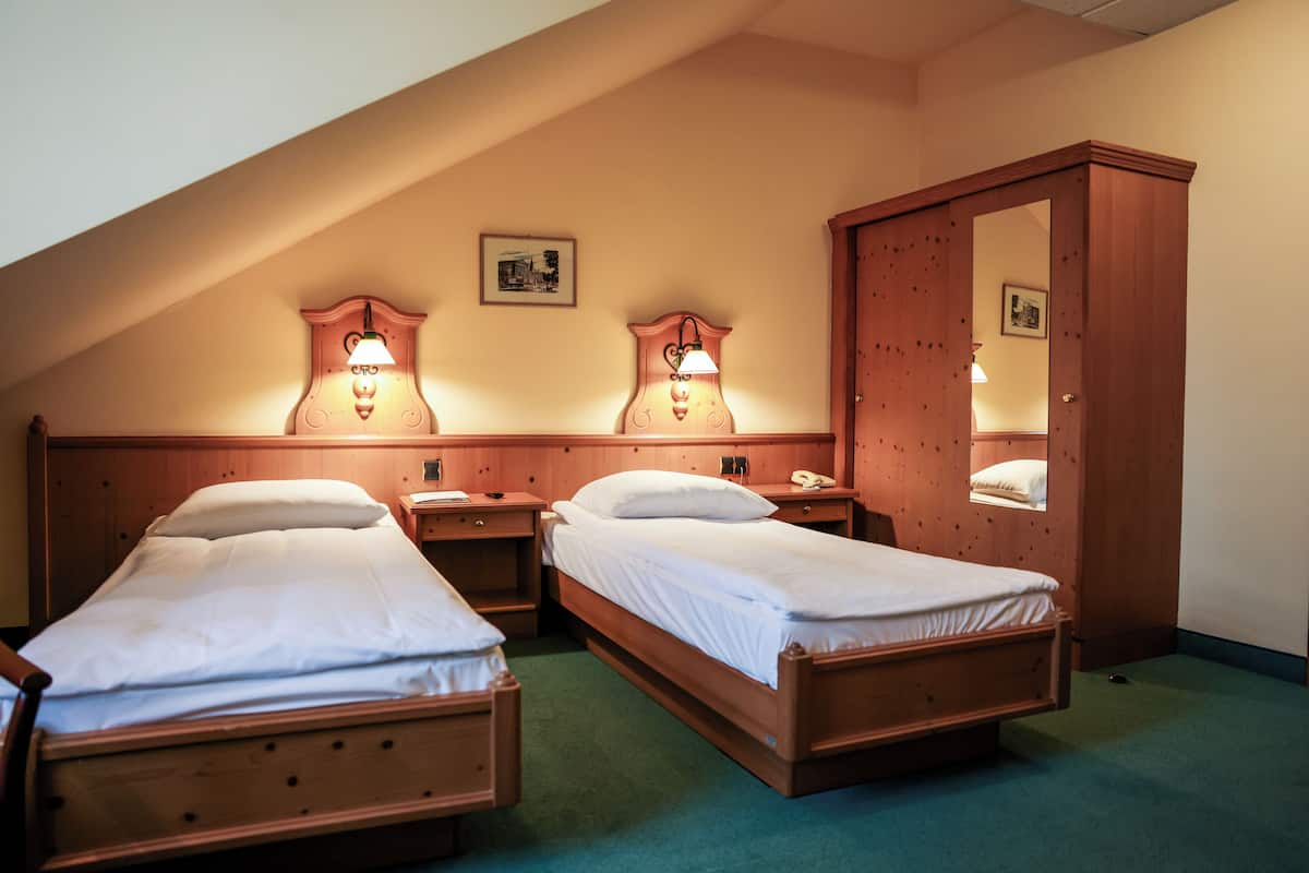 A room with two wooden beds, each with a nightstand and a lamp. There is a wooden wardrobe and a mirror on the wall.