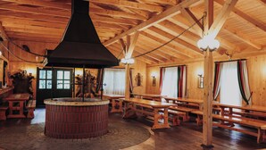 A wooden interior with a central fireplace, benches, and a circular brick structure.