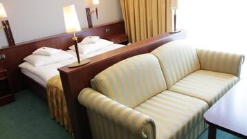 Una habitación de hotel con una cama, un sofá a rayas, una mesita de noche de madera y dos lámparas de noche.