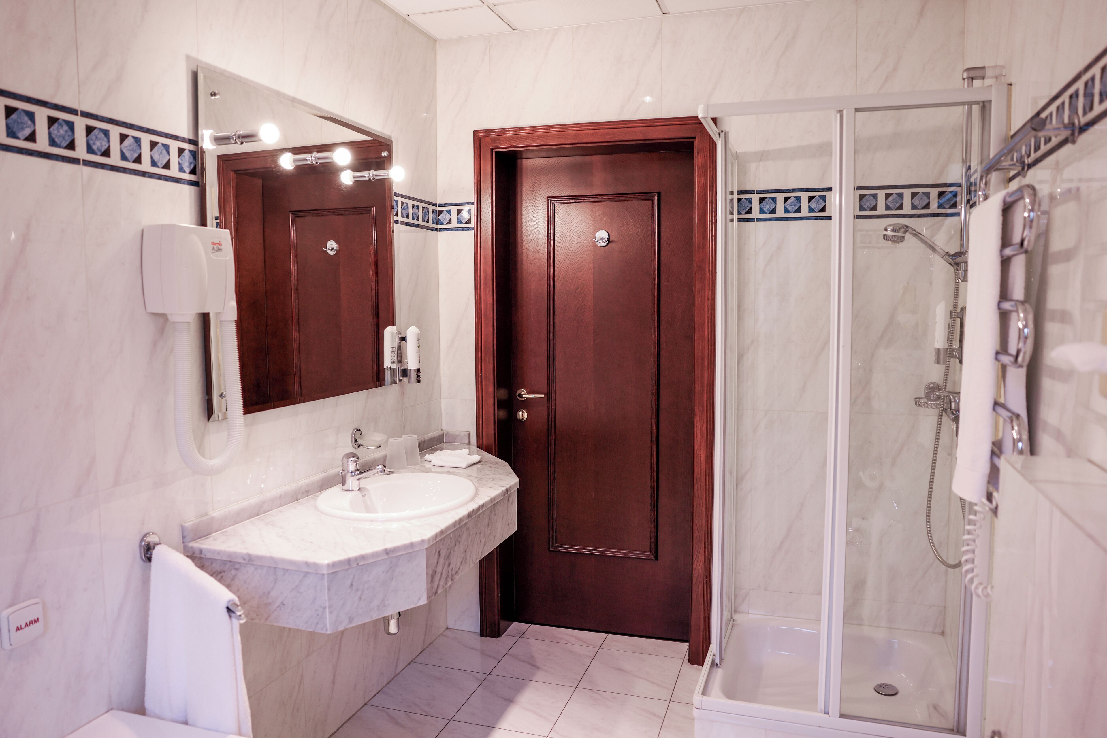Un baño con lavamanos de mármol, puerta de madera y ducha con cerramiento de vidrio.