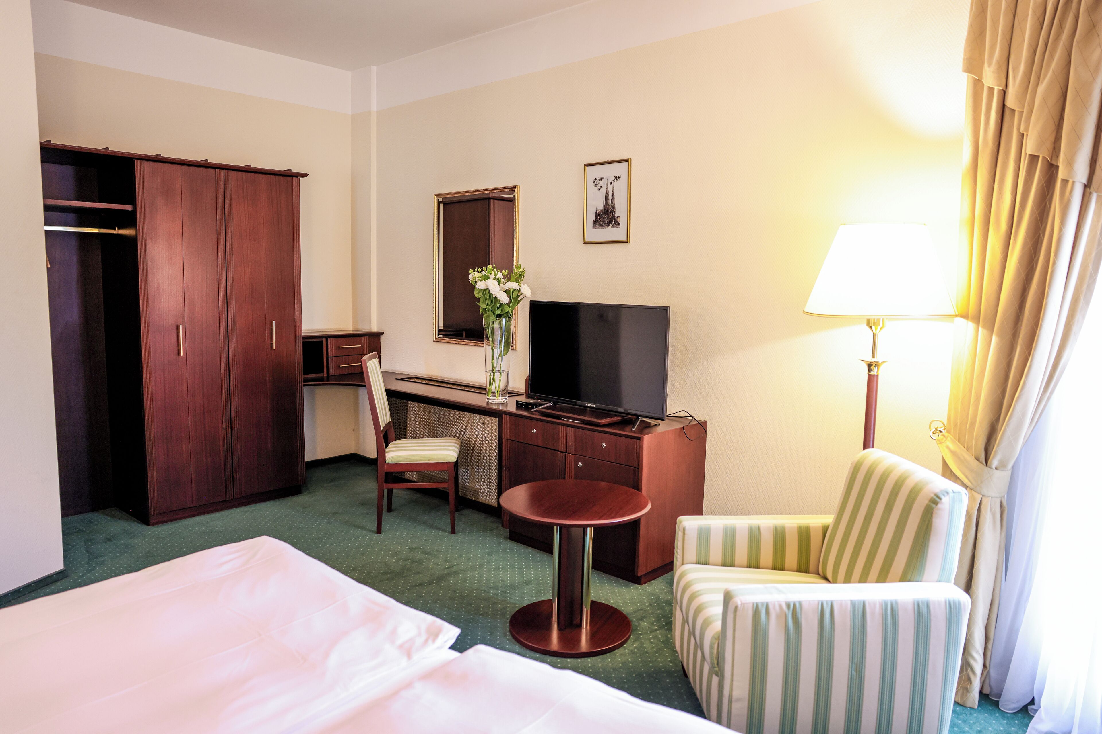 Habitación de hotel con cama, escritorio con televisor, silla, mesita y armario.