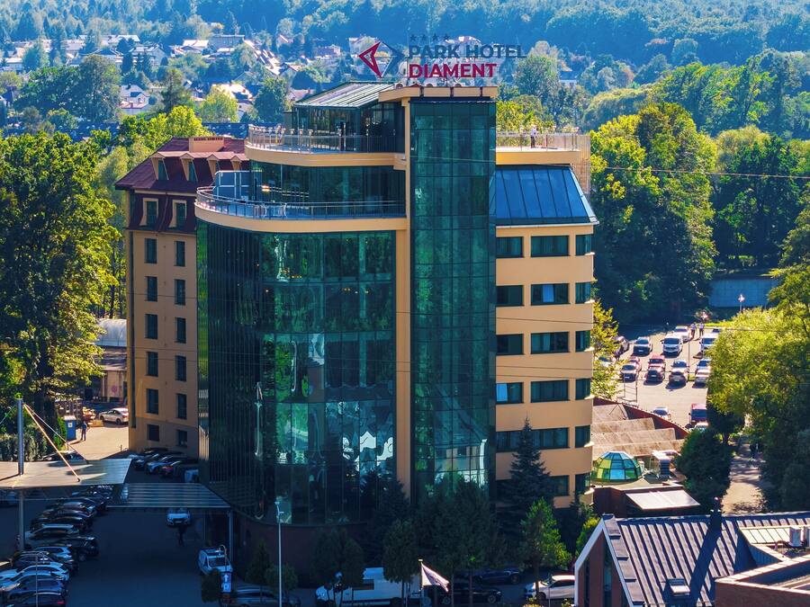 A multi-story hotel with a glass facade, a parking lot, and a view of a residential area in the background.