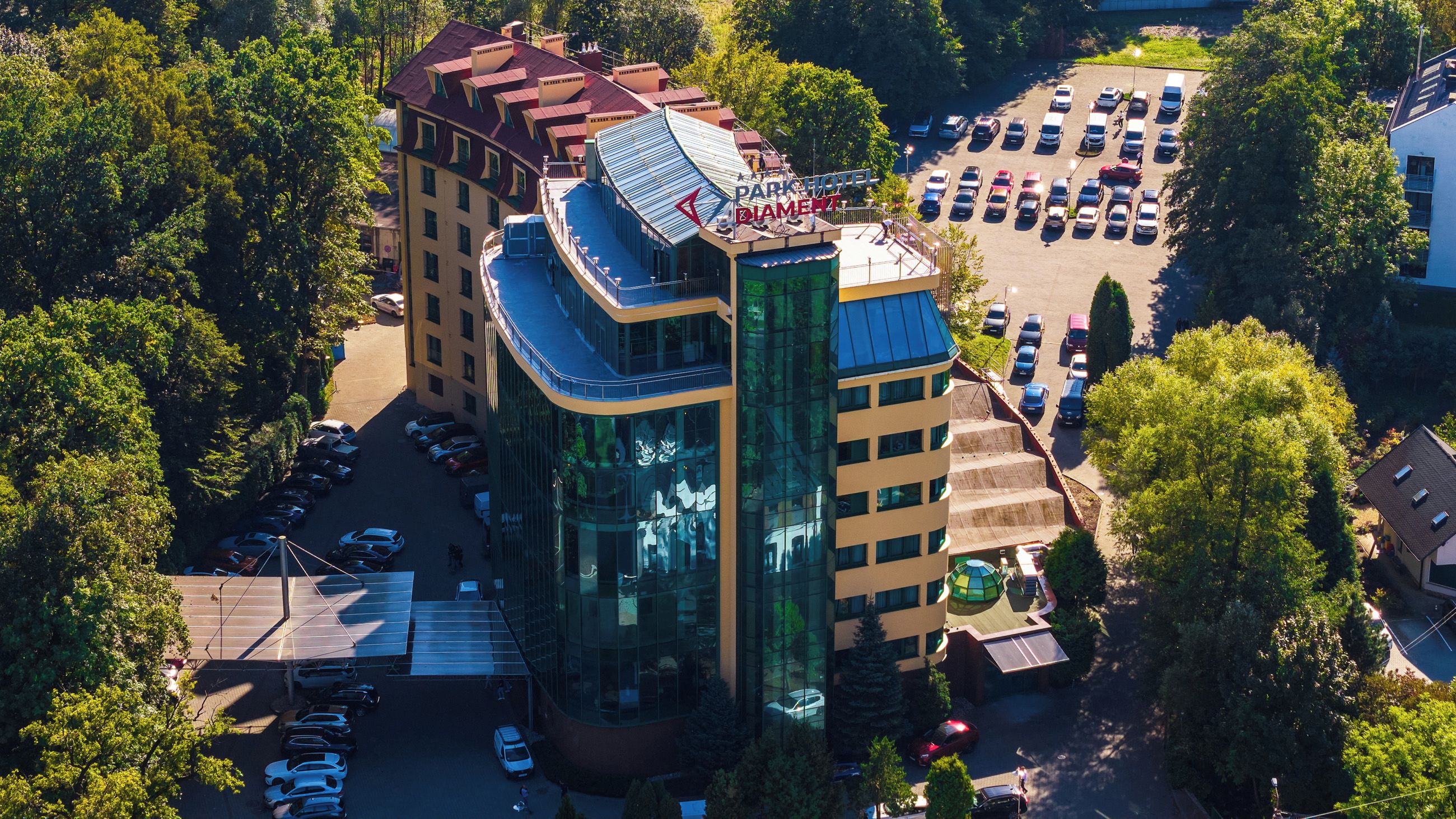 Un hotel de varios pisos con fachada de vidrio moderna, estacionamiento y zonas verdes circundantes.