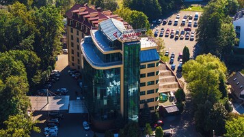 Un hotel de varios pisos con fachada de vidrio moderna, estacionamiento y zonas verdes circundantes.