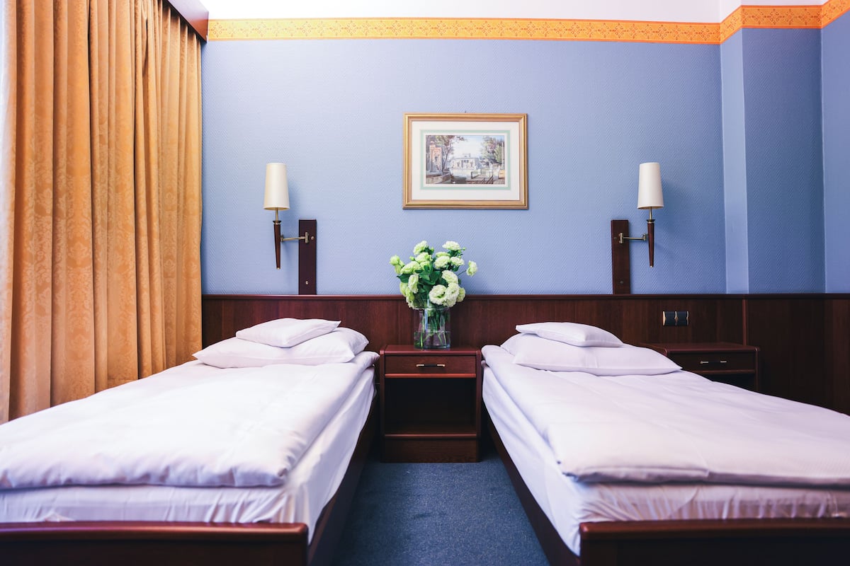 A hotel room with two single beds, a nightstand with a vase of flowers, and a framed picture on the wall.