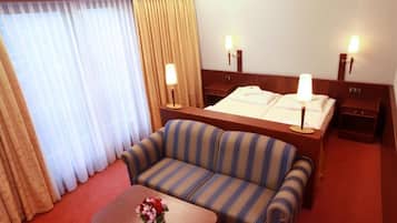 Et hotelværelse med en seng, to sengeborde med lamper, en stribet sofa, et lille bord med en vase blomster og et vindue med gardiner.