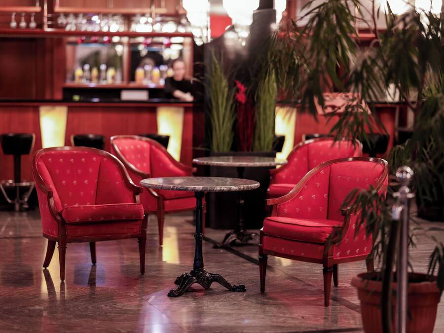 Un área de bar con sillas tapizadas de rojo, una mesa redonda y una barra con una persona al fondo.