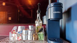 Una cafetera, una botella de vainilla francesa y un soporte para cápsulas de café sobre una encimera.