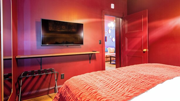 Una habitación con una cama, un televisor en la pared, una puerta y un banco.