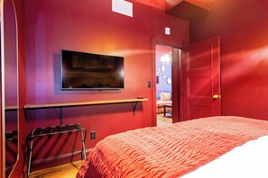 A room with a bed, a TV mounted on the wall, a door, and a bench. - Hollyhock Suite 508: 2 beds/1 bath (Louisville)