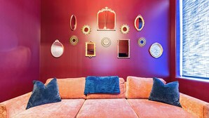 Una habitación con una pared roja, un sofá modular con cojines azules, varios espejos de pared y objetos decorativos.
